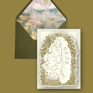 May include: An invitation card with a swan design. The card features a cream-colored illustration of swans surrounded by floral elements. The envelope has a painting of swans on a pond. The background is a muted olive green.