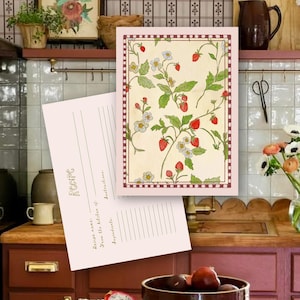 May include: A rectangular recipe card featuring a cream-colored background with a repeating pattern of red strawberries, green leaves, and white flowers, framed by a red and white checkered border. The reverse side is light pink with lined sections.