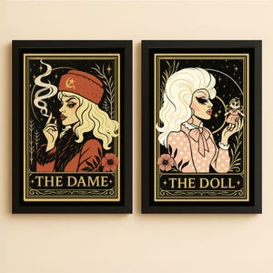May include: Two framed art prints. The left print features a blonde woman in a red hat smoking a cigarette, with the text "THE DAME." The right print shows a blonde woman holding a doll, with the text "THE DOLL."