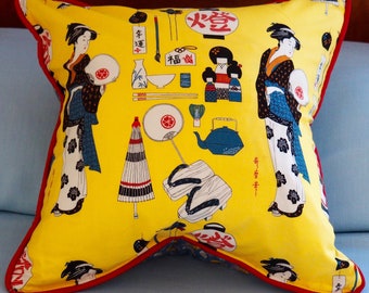 May include: Yellow throw pillow with a red border featuring a Japanese-inspired design. The pillow has images of women in traditional clothing, fans, chopsticks, and other Japanese cultural items. The text on the pillow reads "幸運" and "火箸".