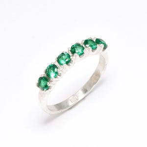 May include: A silver band ring with seven green gemstones set in a row.