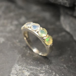 May include: A silver band ring with a row of five opal gemstones. The opals are a mix of white, light blue, and green.