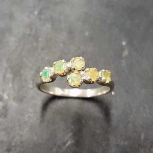 May include: A silver ring with a cluster of six small, round, pale yellow opals set in a curved line.
