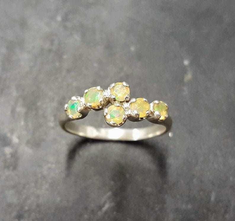 May include: A silver ring with a cluster of six small, round, pale yellow opals set in a curved line.