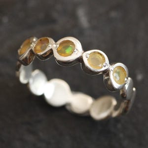 May include: A silver band ring with a row of oval-shaped yellow opals.