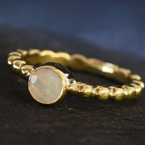 May include: A gold ring with a round, white opal gemstone set in a beaded band.