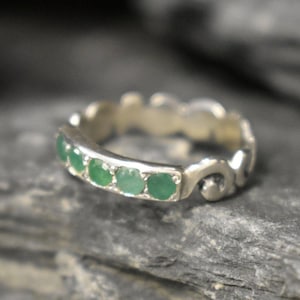May include: A silver ring with a delicate, ornate design and a row of emerald green gemstones.