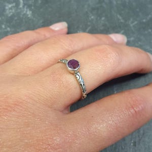 May include: A silver ring with a delicate, swirling design and a small, round, dark red gemstone.