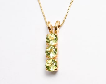 May include: A gold chain necklace with a pendant featuring three green gemstones.