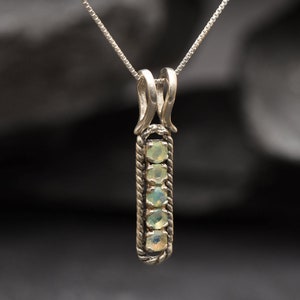 May include: A silver necklace with a pendant featuring five small, round, light green opals set in a silver frame.