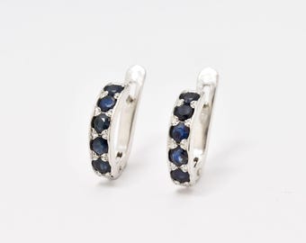 May include: A pair of silver hoop earrings with a row of dark blue sapphires around the hoop.
