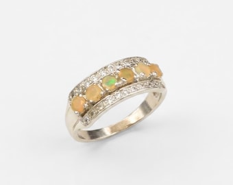 May include: A silver-toned ring featuring a central row of five round, iridescent opals. The band is accented with two parallel rows of small, clear, sparkling stones flanking the opals, creating a multi-layered, polished metal design.