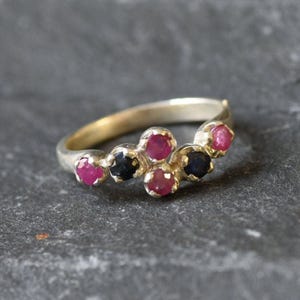 May include: A silver ring featuring a cluster of pink and blue gemstones. The ring has a curved design and is set with five stones.
