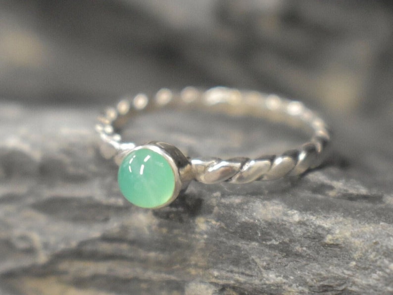 May include: A silver ring with a twisted band and a light green gemstone.