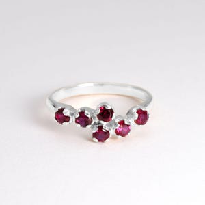 Peut inclure: Une bague en argent avec un groupe de six pierres précieuses rouges disposées en ligne courbe.
