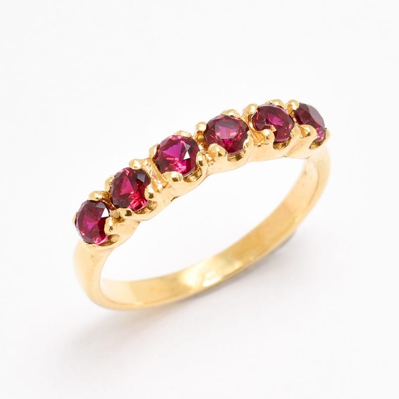 May include: A gold band ring with six red gemstones set in a row.