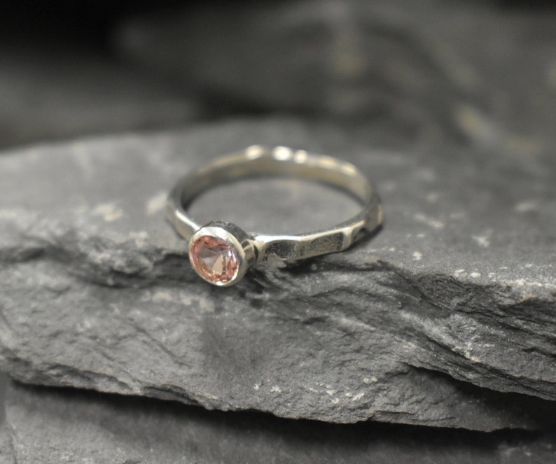 May include: A silver ring with a hammered texture and a pink gemstone set in the center.