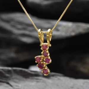 Peut inclure: Un collier en or avec un pendentif composé d'un groupe de petites pierres de rubis rouges.