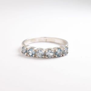 May include: A silver band ring with seven light blue gemstones set in a row.