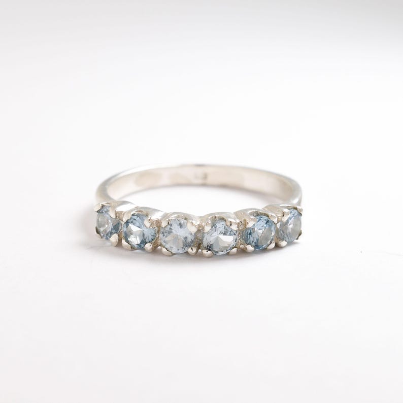 May include: A silver band ring with seven light blue gemstones set in a row.
