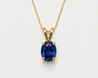 May include: A gold necklace featuring a central oval-cut deep blue gemstone pendant held by a four-prong setting. The pendant is suspended from a delicate gold box chain, creating a refined and classic piece of jewelry with a polished finish.