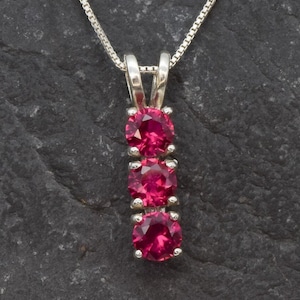 May include: A silver necklace with a pendant featuring three round, pink gemstones.
