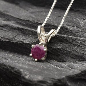 Peut inclure: Un collier avec un pendentif en argent orné d'une pierre de rubis ronde de couleur rouge foncé.