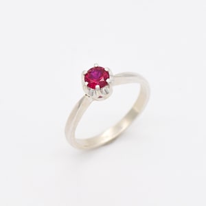 Peut inclure: Une bague en argent avec une seule pierre précieuse rouge sertie à griffes.