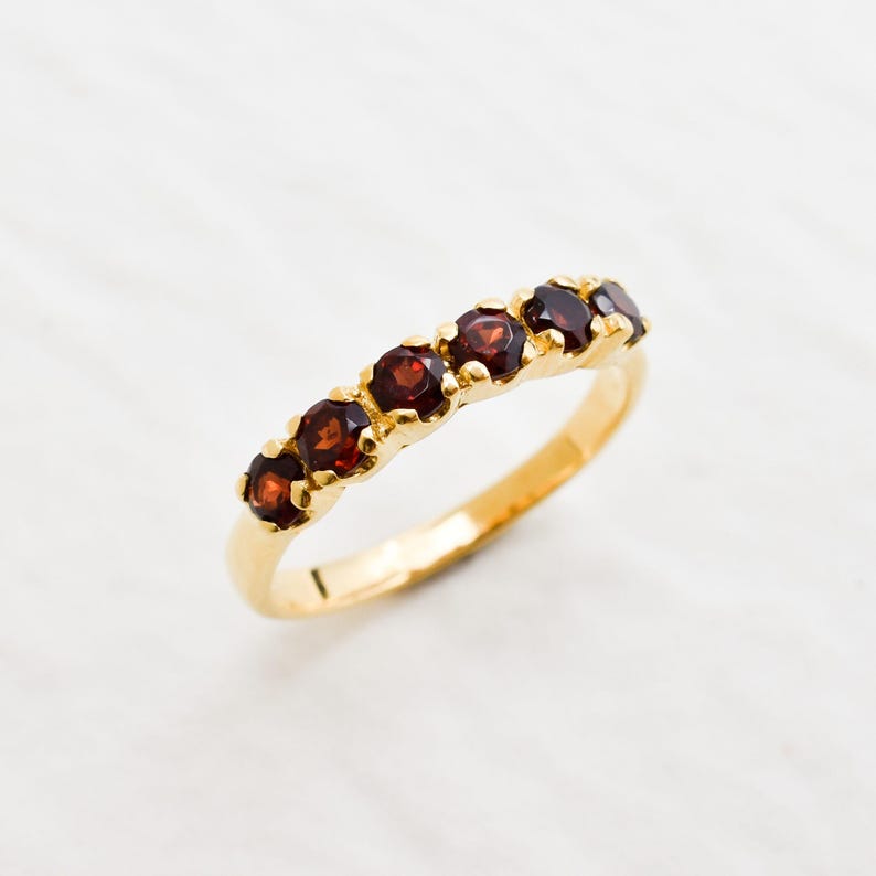 May include: A gold band ring with six red gemstones set in a row.