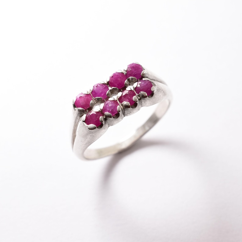 May include: A silver ring with a row of pink gemstones set in the band.