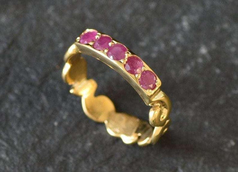 May include: A gold band ring with a row of pink ruby stones set in the band.