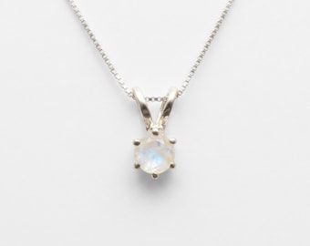 May include: A silver necklace with a small, round, iridescent gemstone pendant. The pendant is held in place by six prongs. The chain is a delicate box chain. The gemstone has a soft, milky appearance with hints of blue and white.