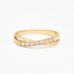 May include: A gold band ring with a row of small clear diamonds set in a criss-cross pattern.