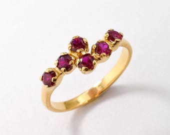 May include: A gold ring with a curved row of six ruby red gemstones.