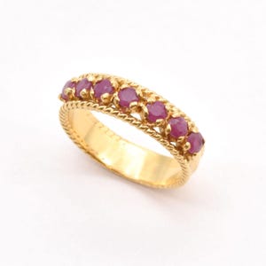 Könnte beinhalten: Ein Goldring mit einer Reihe von rosafarbenen Rubin-Steinen, die in einem seilartigen Design eingefasst sind.
