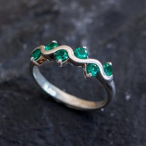 Puede incluir: Un anillo de plata con una banda ondulada y cinco piedras preciosas de color verde esmeralda.