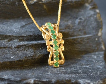 May include: A gold pendant necklace with a delicate, ornate design featuring a row of emerald green gemstones.