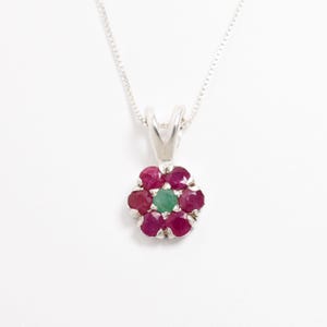 May include: A silver necklace with a flower pendant featuring red rubies and a green emerald in the center.