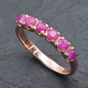 May include: A rose gold band ring with six pink ruby gemstones set in the band.
