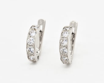 May include: A pair of silver hoop earrings. Each earring features a row of clear, sparkling gemstones set along the front. The earrings are displayed against a plain white background, highlighting their design and details.