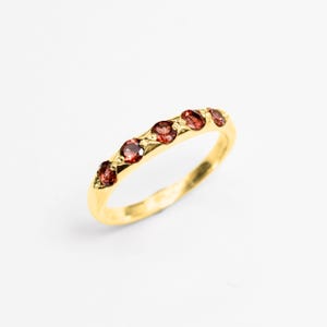 Op de afbeelding: Een gouden ring met zes rode edelstenen in een delicaat patroon.