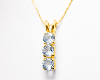 May include: A gold chain necklace with a pendant featuring three round, light blue gemstones.