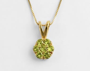 May include: A gold-colored necklace with a pendant featuring a cluster of small, round, light green gemstones. The pendant is flower-shaped and set in a gold-colored metal. The chain is a delicate, gold-colored link chain.