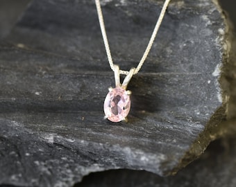 May include: A delicate silver chain necklace with a pink oval gemstone pendant.