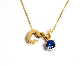 May include: A gold chain necklace with a pendant featuring the letter "C" and a blue gemstone.