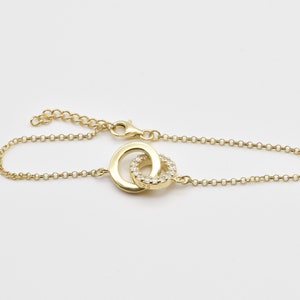 May include: A gold chain bracelet with a double circle pendant. The circle pendant is set with small clear stones.