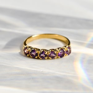 May include: A gold band ring with a row of six purple amethyst gemstones.