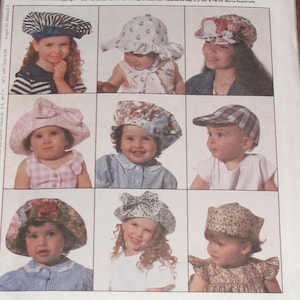 May include: Nine different baby hats are displayed in a grid. The hats vary in style, including bonnets, caps, and sun hats, and feature a variety of patterns and colors, such as stripes, floral prints, and solid colors. The image is a pattern from The McCall Pattern Co.