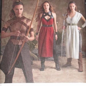 May include: Simplicity sewing pattern 8074 features three costume designs. The cover shows women in warrior-style outfits, including a dress with a crisscross bodice, a red dress, and a white dress with a belt. The pattern size is US 6-14.