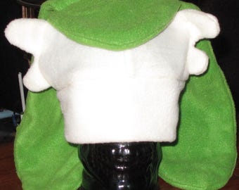 Puede incluir: Un gorro de felpa verde y blanco con orejas puntiagudas. El gorro tiene una parte delantera blanca, una parte superior verde y solapas para las orejas verdes. El gorro está hecho de un material suave y difuso.